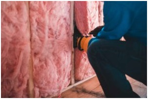 Technician installing pink fiberglass batt insulation in a wall.